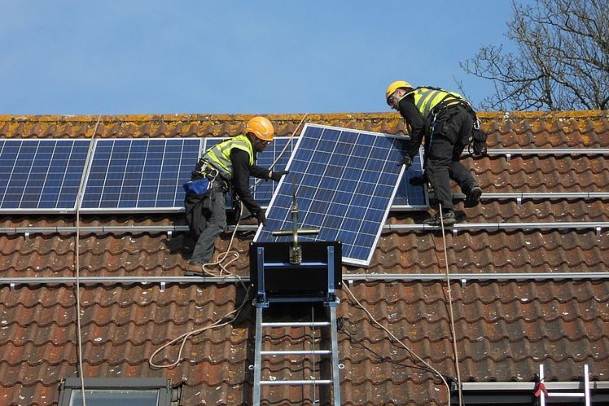 A photo of 2 men installing solar panels using a geda rope hoist